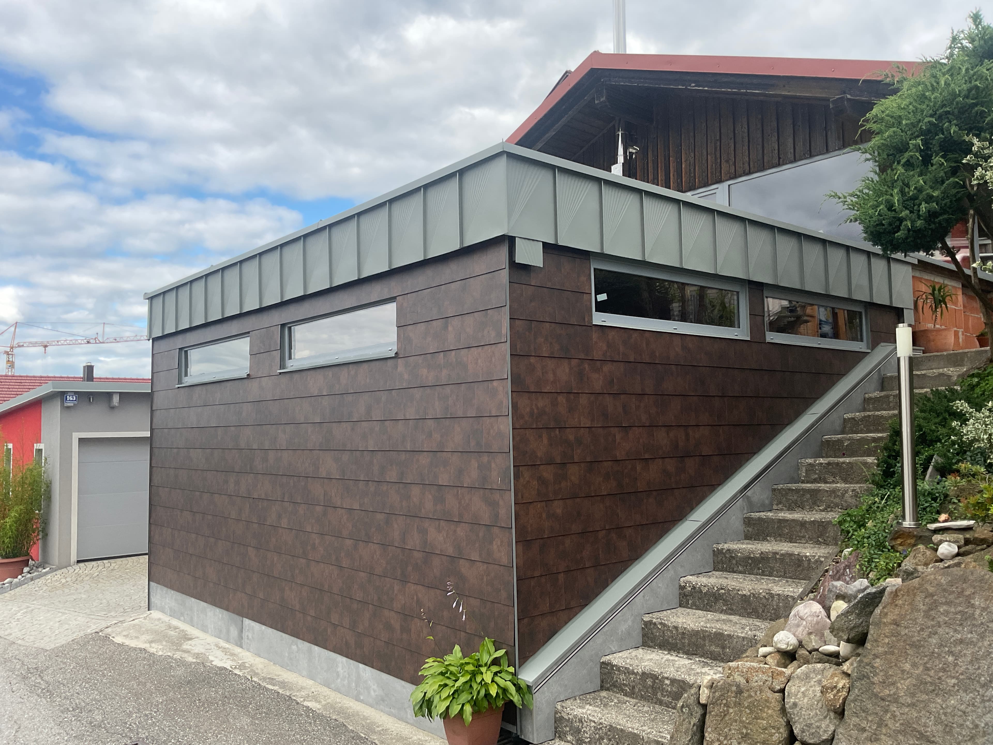 Moderne Garage mit dunkler Wandverkleidung und Stehfalz-Attika